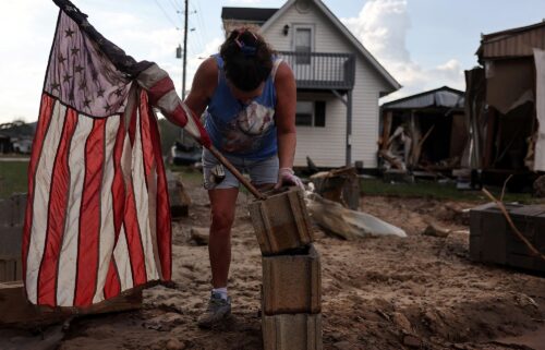 Roxanne Brooks mounts an American flag to a stack of cinderblocks outside her friend's destroyed mobile home (R) in the aftermath of Hurricane Helene flooding on October 6 in Swannanoa