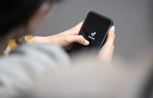 A teenager looks at a smartphone with the TikTok logo displayed. A bipartisan group of 14 attorneys general from across the country filed lawsuits on October 8 against TikTok