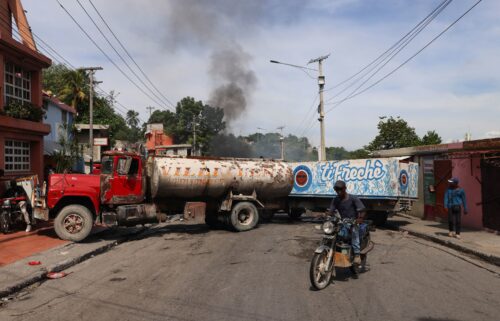 A motorcyclist drives around trucks blocking the road as heavily-armed gangs