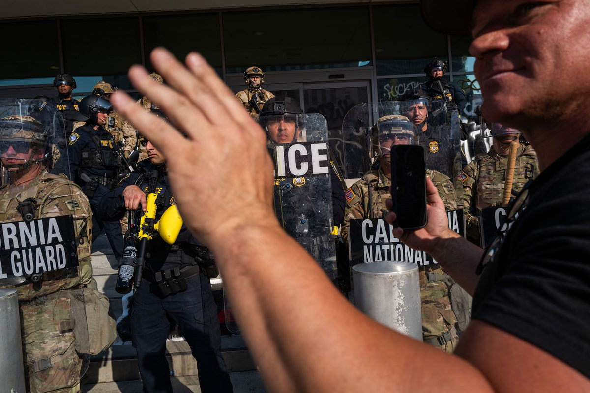 <i>Spencer Platt/Getty Images via CNN Newsource</i><br/>A person holds up their phone in front of the National Guard and police as they confront protesters following three days of clashes with police after a series of immigration raids on June 9 in Los Angeles.
